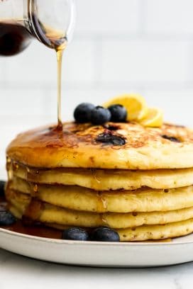 Pouring maple syrup onto Blueberry Lemon Ricotta Pancakes on a plate