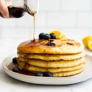 Pouring maple syrup onto Blueberry Lemon Ricotta Pancakes on a plate