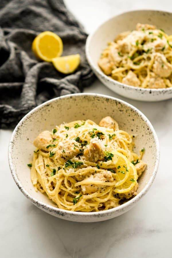 Two bowls of spaghetti pasta tossed with chicken pieces n creamy lemon sauce, topped with parmesan cheese 