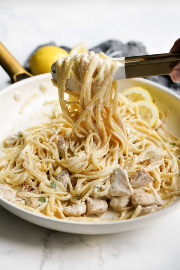Lifting up creamy linguini with a tongs, pasta is tossed with lemon creamy sauce and chicken