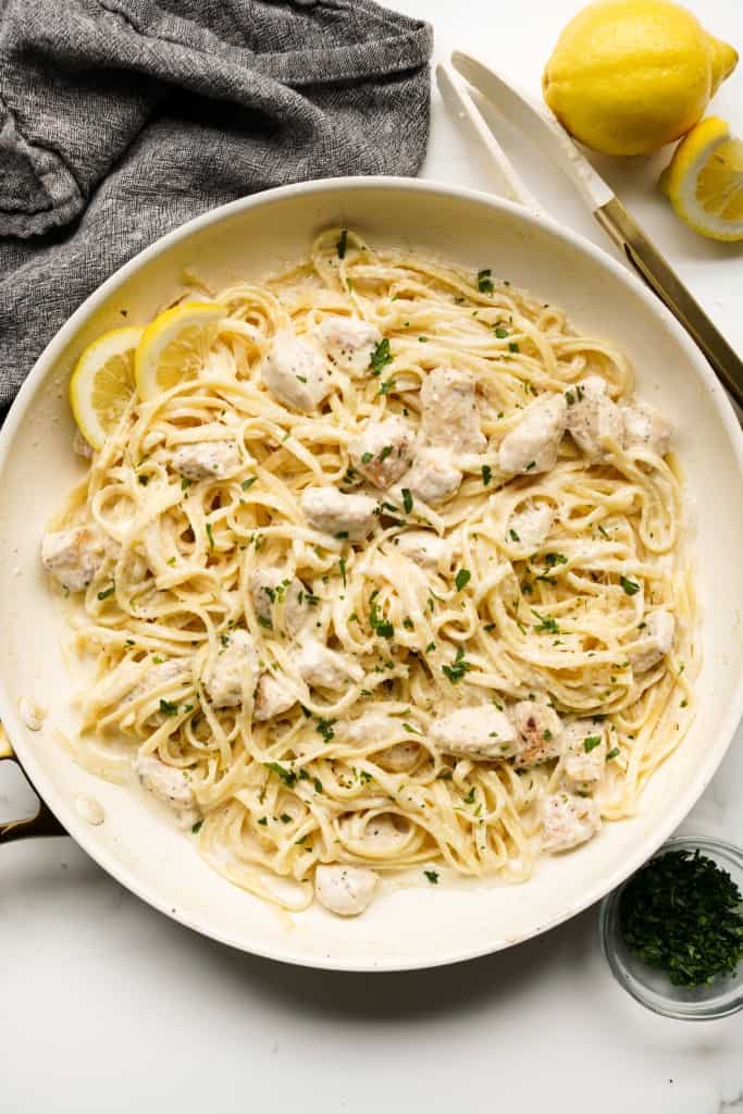 Top down view of creamy lemon chicken pasta topped with parmesan and parsley, with lemon wedges on the side
