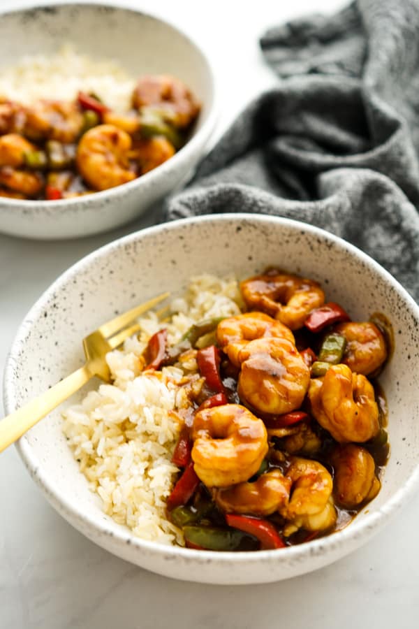 Two bowls of rice topped with General Tso Shrimp bell peppers.