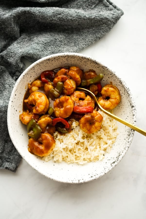 A bowl of shrimp and bell peppers tossed in general tso sauce on top of rice