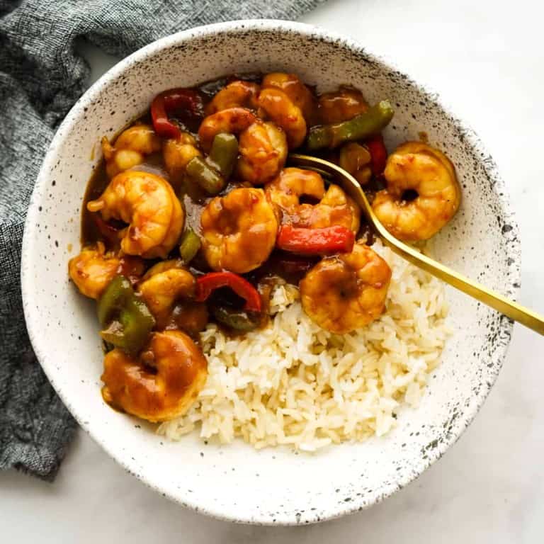 A bowl of shrimp stir fry with bell peppers and sticky sauce on top of rice