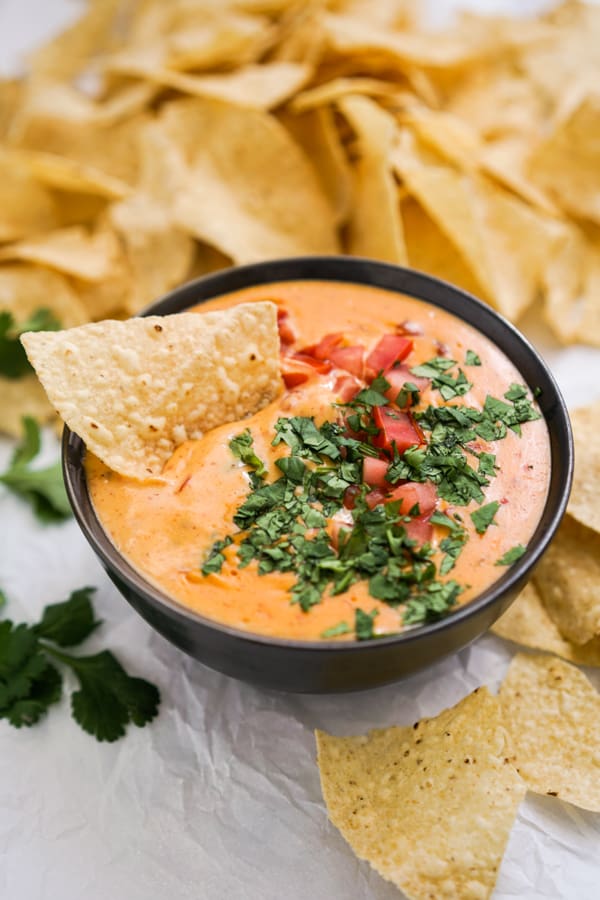 Tortilla chip in a bowl of queso with more chips surrounding it