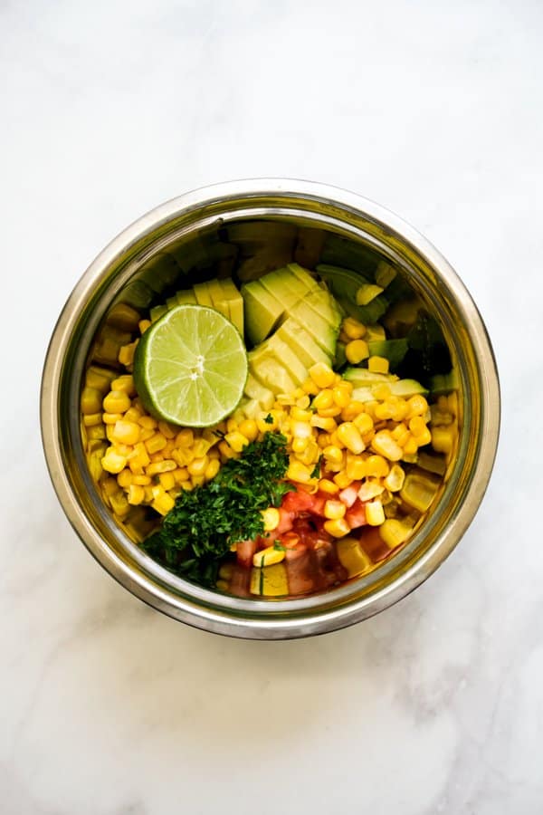 A mixing bowl with corn, tomatoes, cilantro, lime and avocados