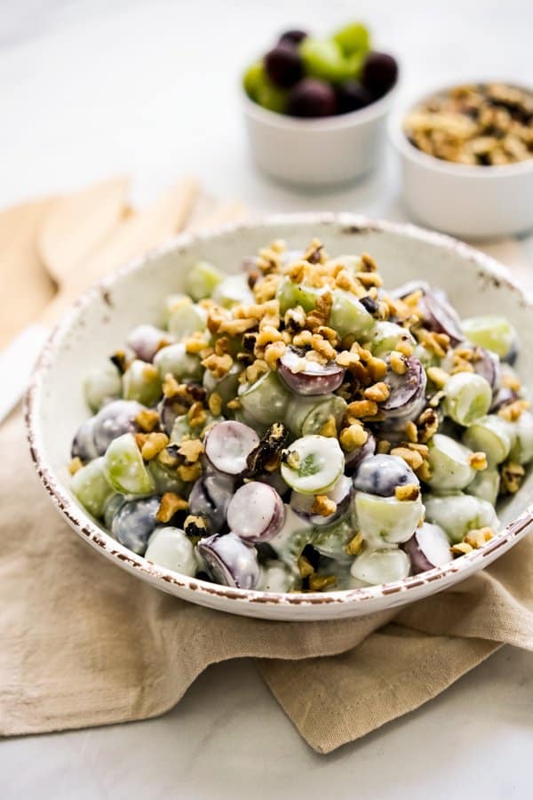 A bowl of grape salad with walnutes, with more grapes and walnuts in the background