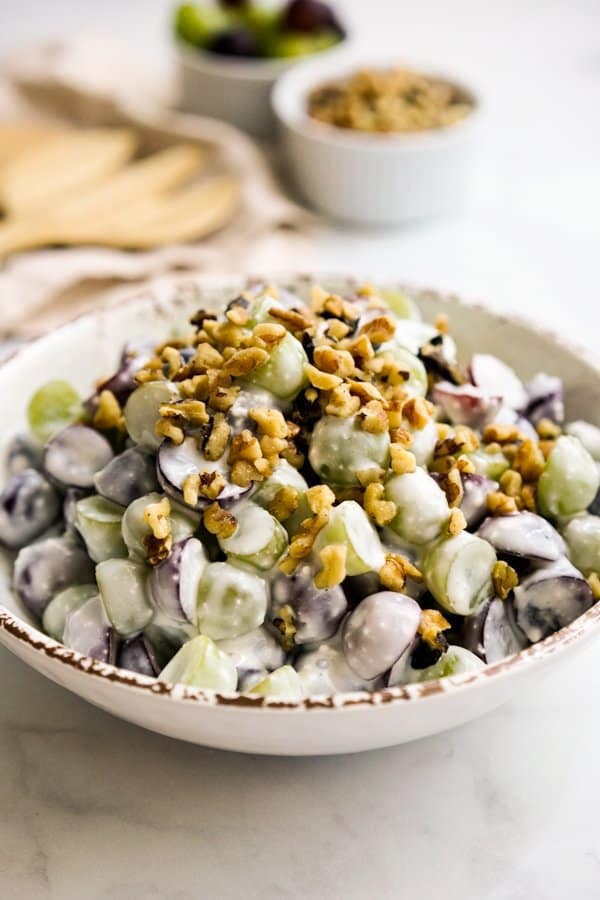 A bowl of green and purple grapes tossed in cream cheese dressing topped with walnuts