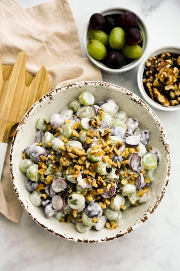 Top down view of a bowl of grapes salad tossed in creamy sauce, with walnuts on top