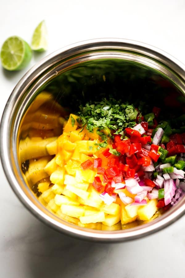 A bowl of pineapples, mangoes, red bell pepper, red onions, cilantro