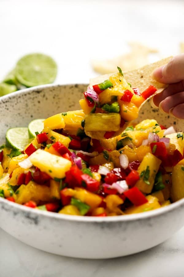 Dipping tortilla chips into a bowl filled with pineapple chunks, mango chunks and bell peppers
