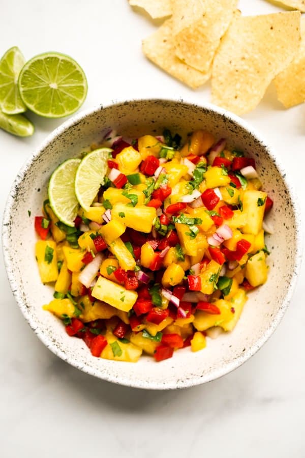 A bowl of Pineapple Mango Salsa with lime wedges on the side