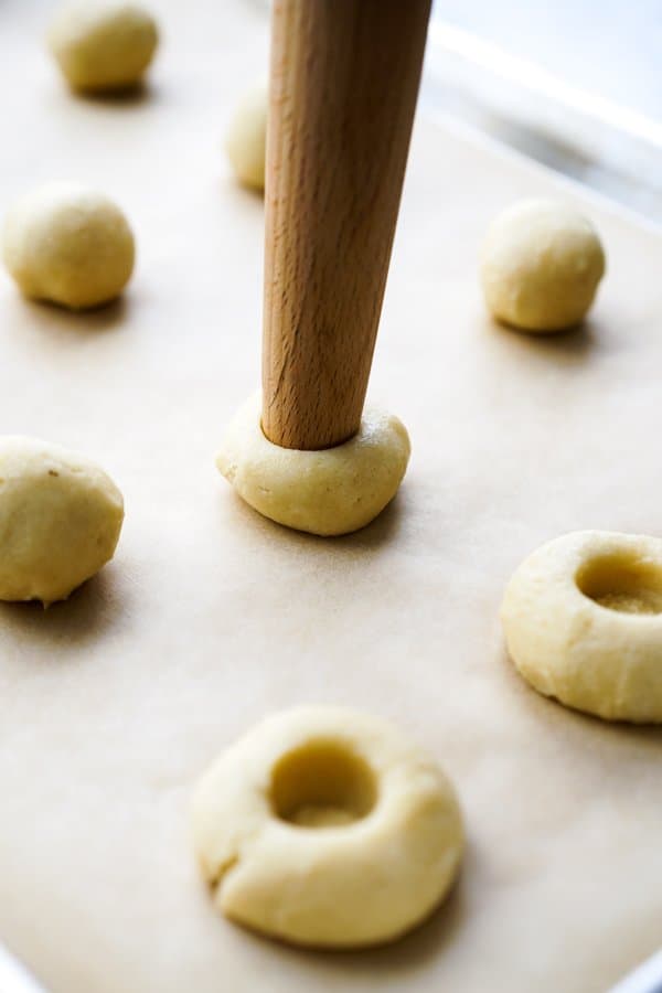 Making an indentation onto the middle of cookie dough ball with a rolling pin