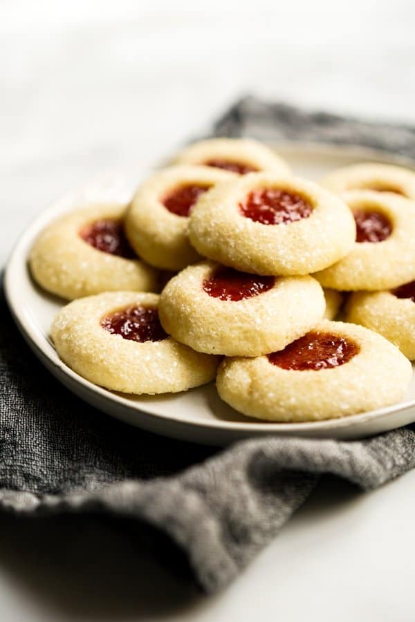 Shortbread thumbprint cookies filled with strawberry jam stacked on a plate