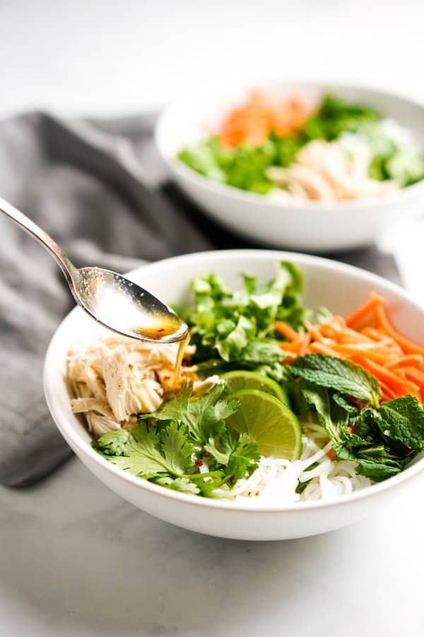 Adding sauce to a bowl of vermicelli rice noodles, carrots, lettuce, and shredded chicken  