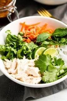 A bowl of rice noodles topped with lettuce, cilantro, mint leaves, carrots and chicken