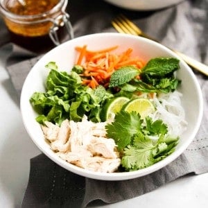 A bowl of rice noodles topped with lettuce, cilantro, mint leaves, carrots and chicken