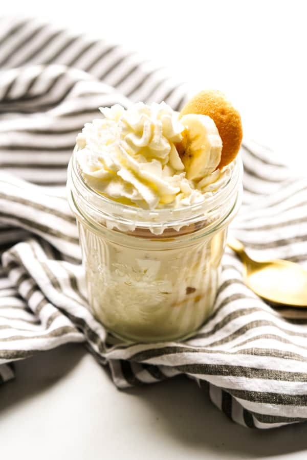 Layers of banana pudding in an individual jar topped with whipped cream, bananas and wafers