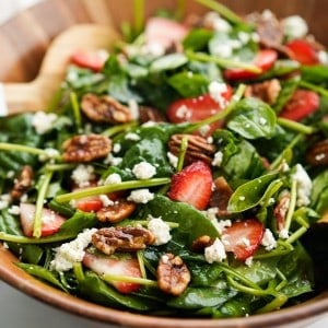 a spinach salad tossed with sliced strawberries, pecans, bacon and blue cheese