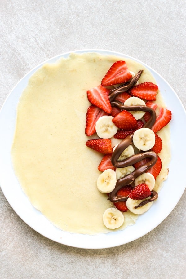 Adding strawberries, bananas and drizzles of nutella onto crepe