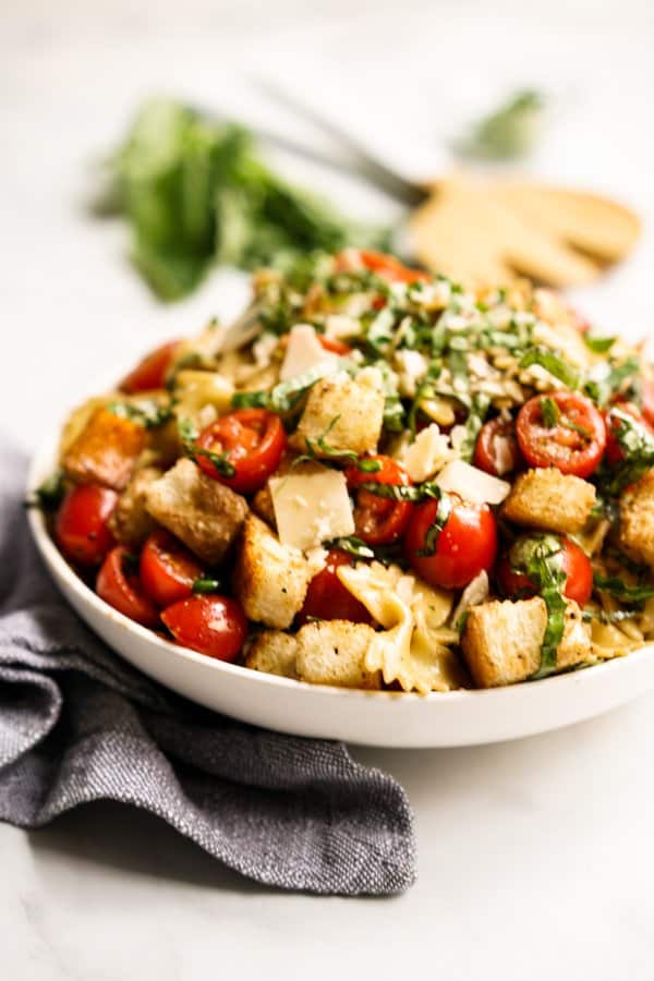 A plate of pasta salad with croutons, tomato, basil and parmesan