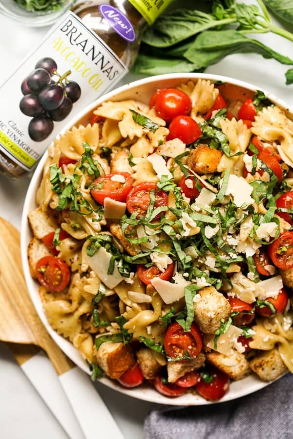 A bowl of pasta salad with tomatoes, basil and parmesan, with salad dressing on the side