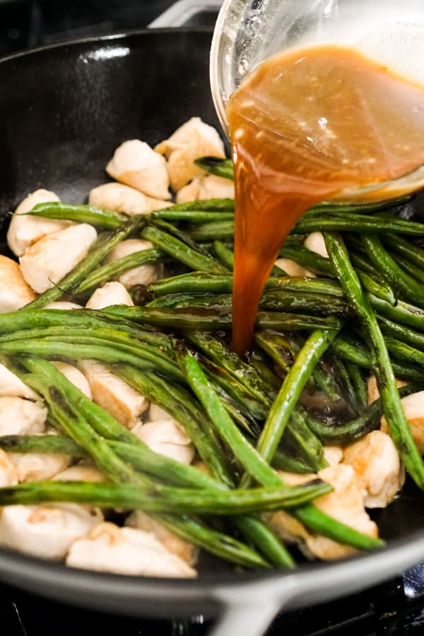 Adding Teriyaki Sauce to chicken and green beans in a skllet