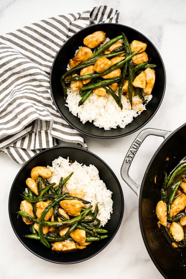 Top down view of two bowls of chicken and green beans, and a pan filled with it