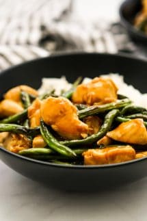 A bowl of rice topped with chicken and green beans in teriyaki sauce