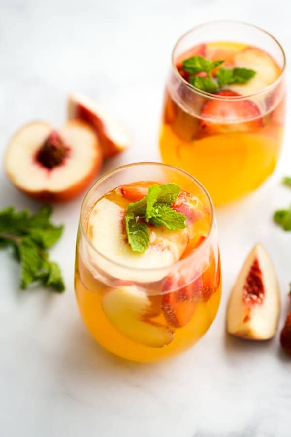 Two glasses of peach sangaria with slices of peaches around it