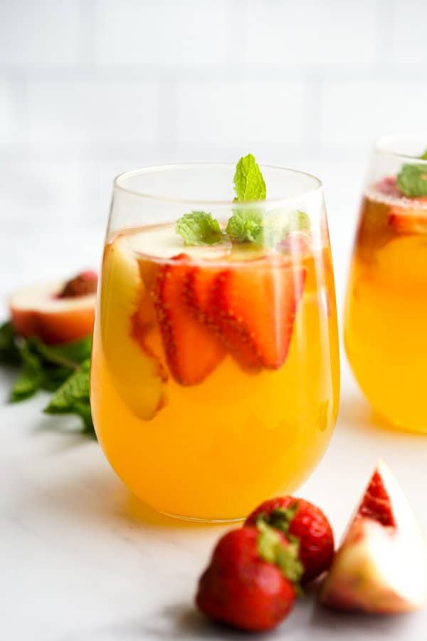 A glass of white wine sangria with fruits and mint on it