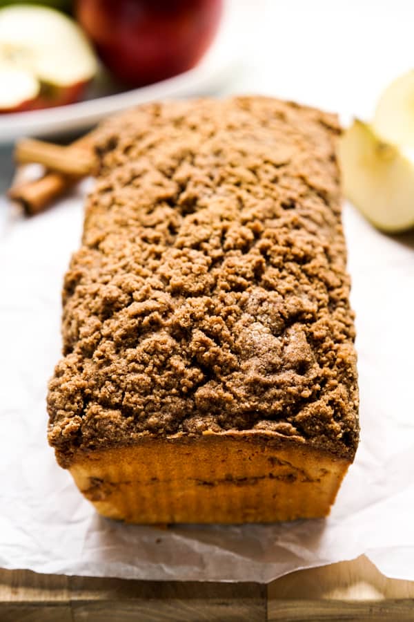 A loaf of Cinnamon Apple Bread with apples in the background