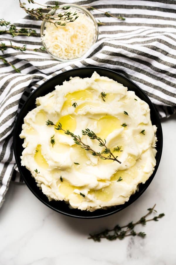 Top down view of a black bowl of mascarpone mashed potatoes topped with herbs