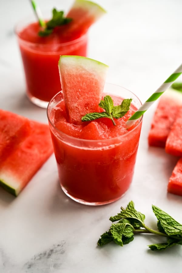 Two glasses of watermelon slush with a straw and a slice of watermelon in it