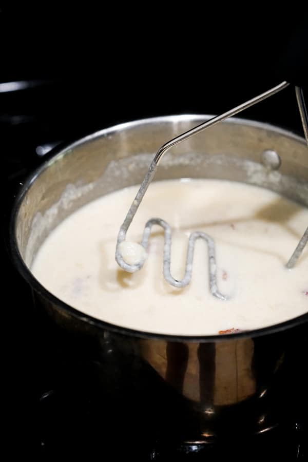 Mashing potatoes in soup with potato masher