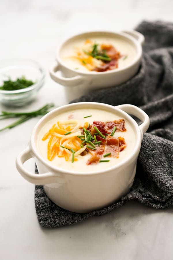 Two bowls of Creamy Potato Bacon Soup with chives in the background
