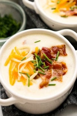 A bowl of potato soup topped with bacon, cheese and chives