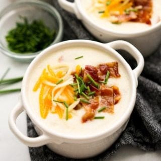 A bowl of potato soup topped with bacon, cheese and chives