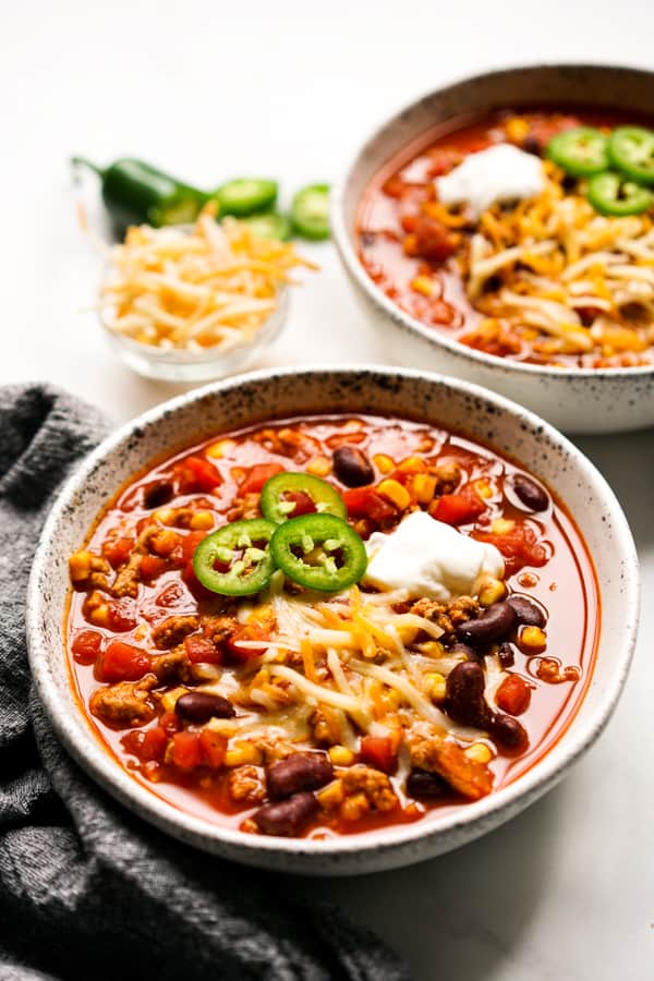 Two bowls of turkey chili with cheese, jalapeño, and sour cream as garnish 