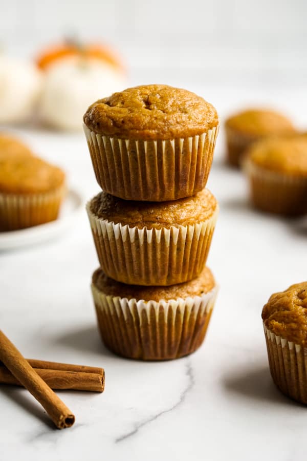 A stack of three muffins with pumpkin in the background