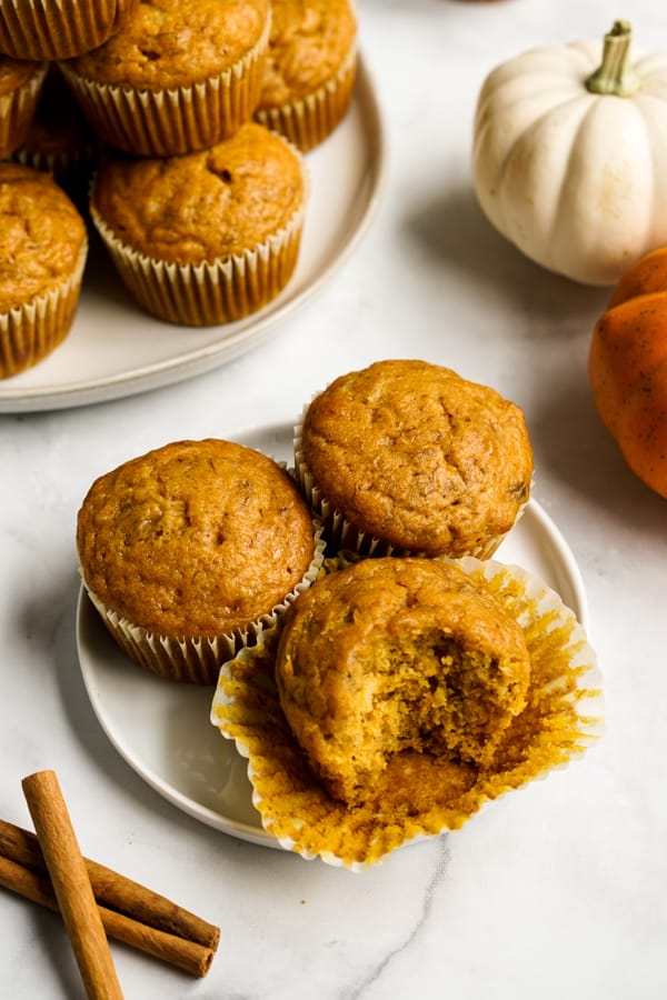 A half eaten muffin on a plate along with other muffins