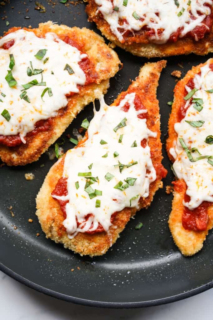 3 pieces of chicken parmesan topped with tomato sauce and cheese in a skillet