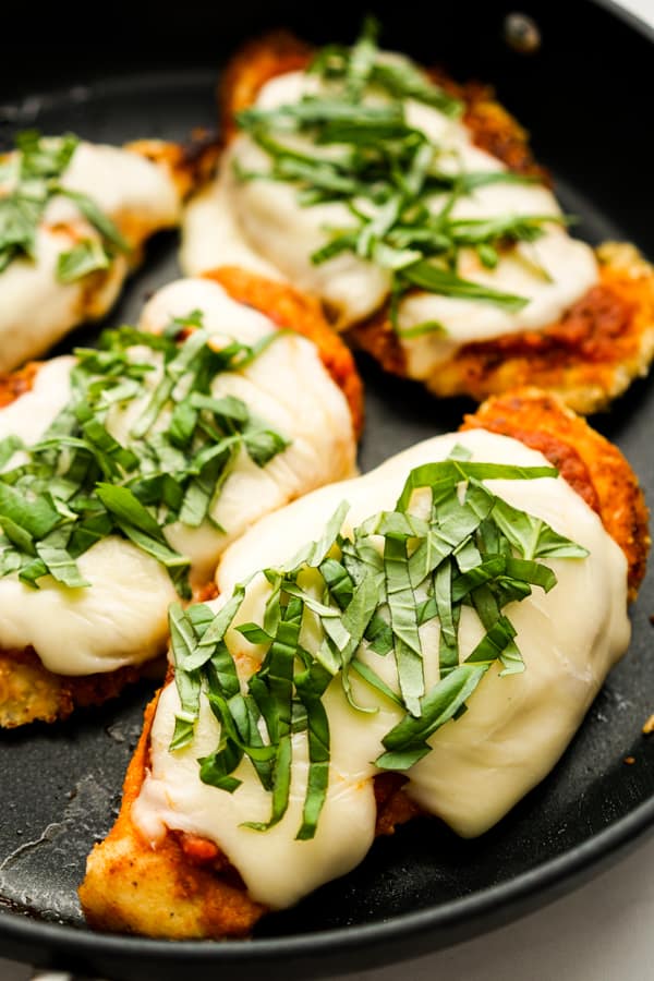 Closeup of chicken parmesan topped with marinara sauce, melted cheese and fresh basil