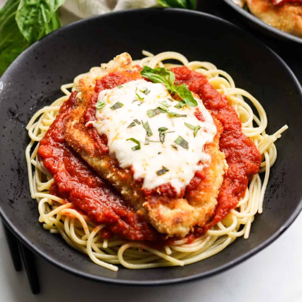 A bowl of spaghetti topped with crispy chicken parmesan with marinara sauce and melted mozzarella cheese on top
