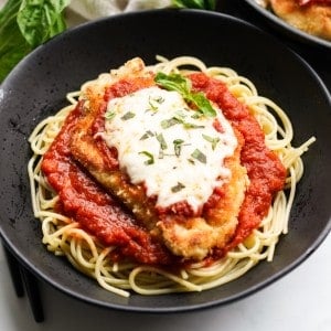 A bowl of spaghetti topped with crispy chicken parmesan with marinara sauce and melted mozzarella cheese on top