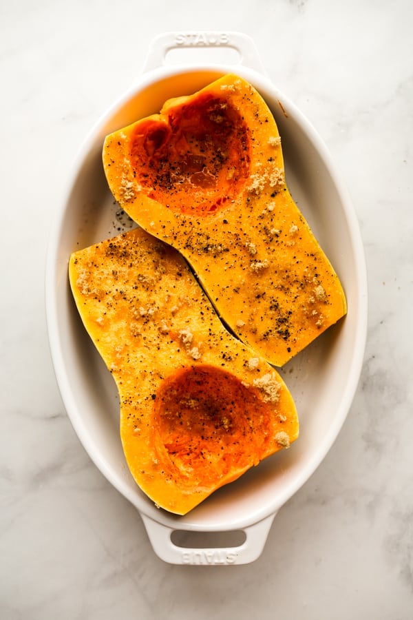 Halved whole butternut squash topped with salt, pepper, brown sugar and olive oil