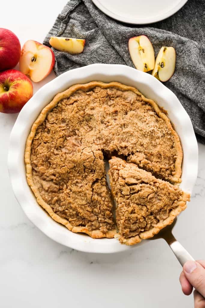 Taking a slice out of a round apple pie in a pie dish topped with crumble topping