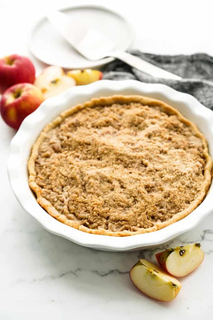 Whole Apple crumble pie in a pie dish, with apples in the background