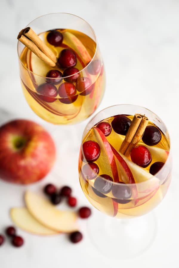 Two glasses of apple cider sangria with cinnamon sticks, apples and pomegranate