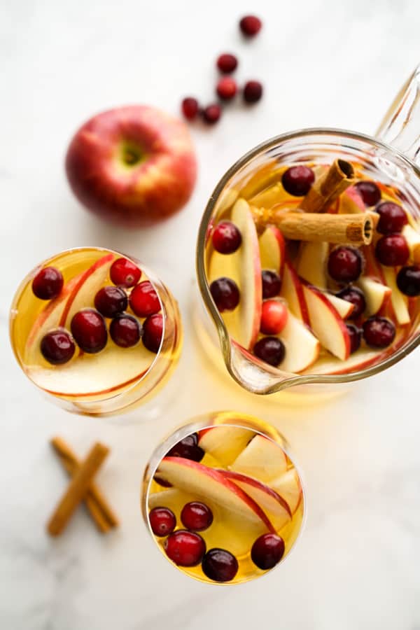 Top down view of cranberries, cinnamon sticks and apples in glasses and a jug of sangria